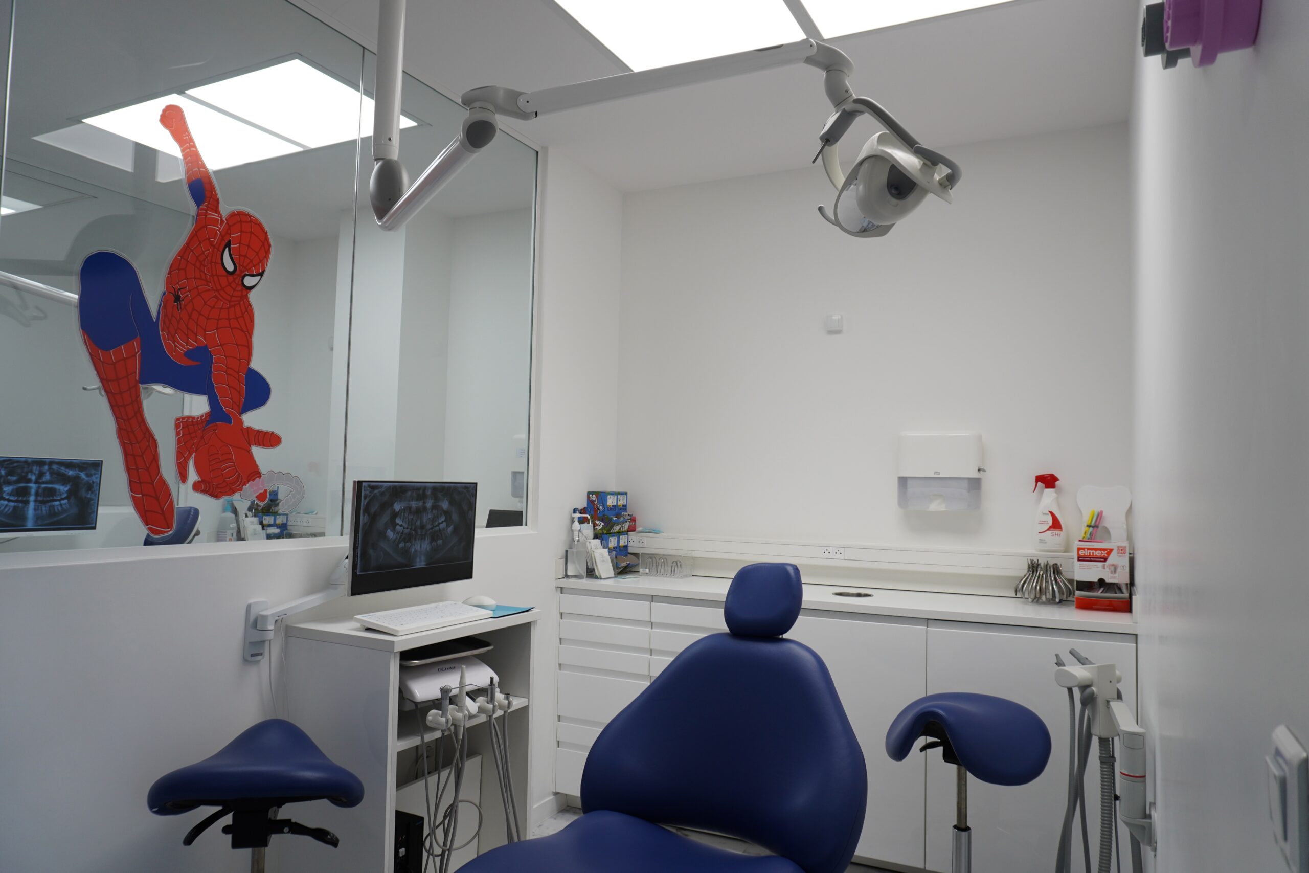 Salle de soins en cabinet d’orthodontie avec fauteuil dentaire, écran de radiographie et décoration murale ludique pour enfants.