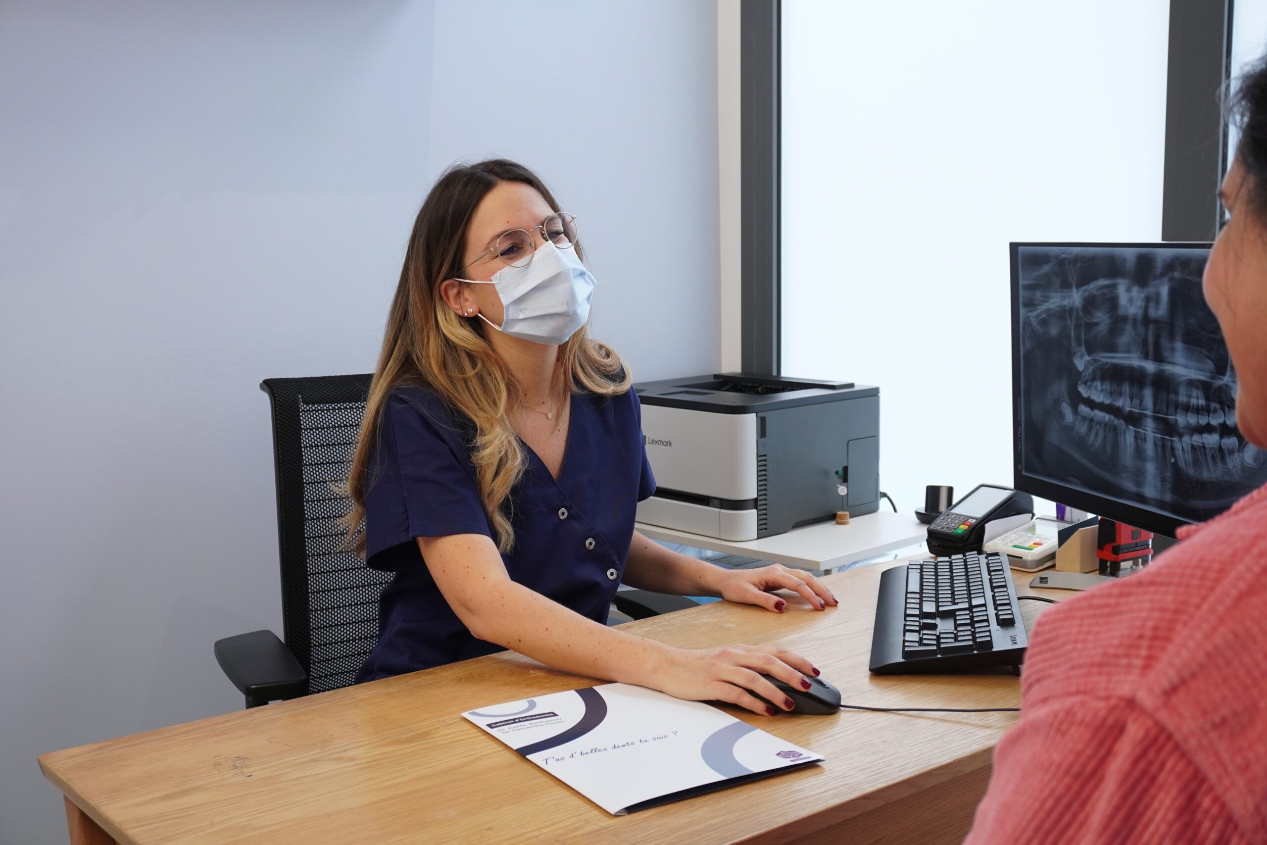 Consultation orthodontique au cabinet avec analyse d’une radiographie panoramique dentaire affichée sur l’écran.