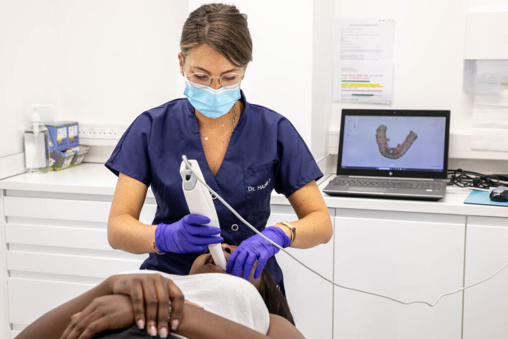 Orthodontiste réalisant un scan intra-oral pour empreinte numérique chez une patiente, avec modélisation 3D des arcades dentaires affichée à l’écran.
