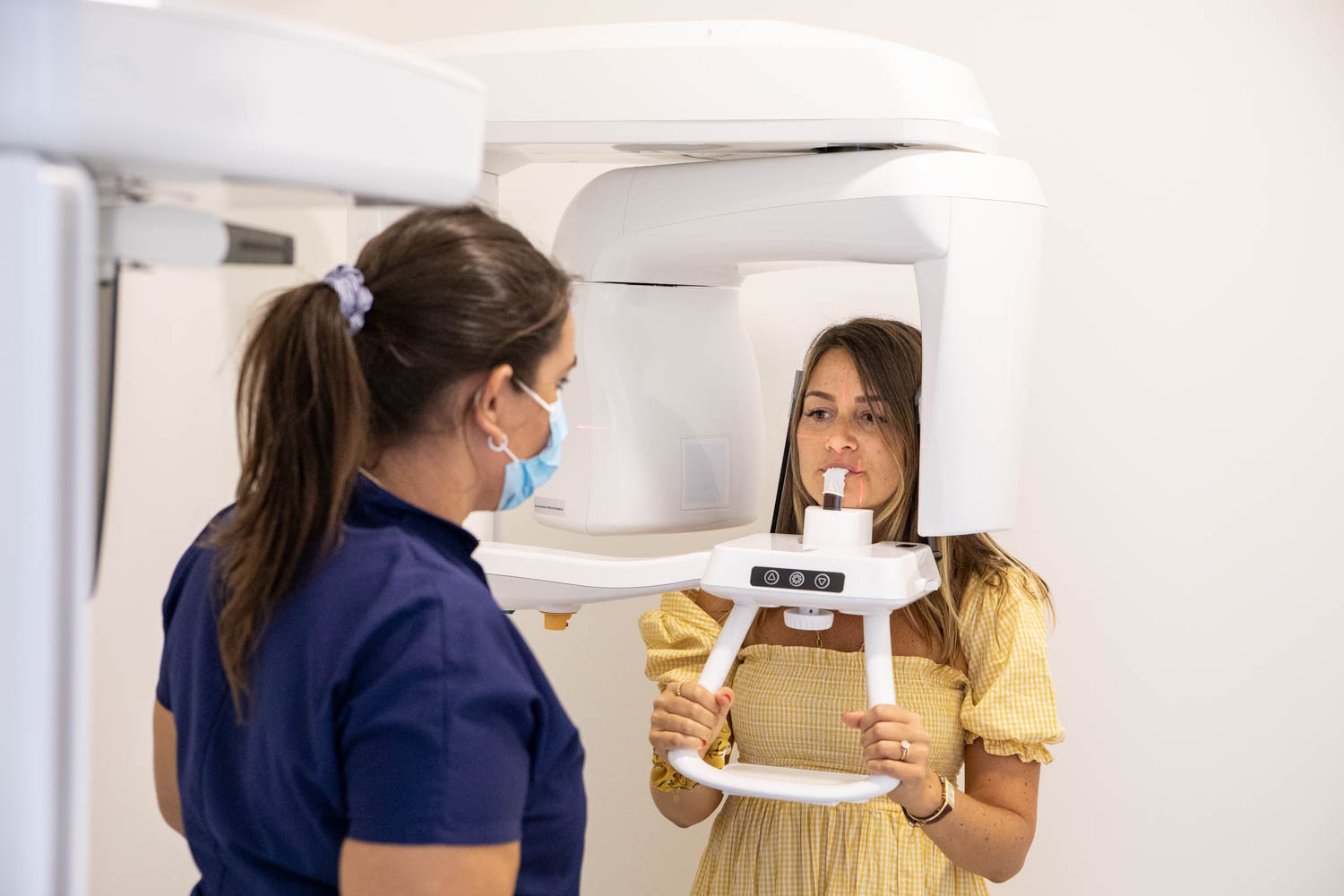 Patiente réalisant une radiographie panoramique dentaire (orthopantomogramme) sous la supervision d’une assistante en cabinet d’orthodontie.