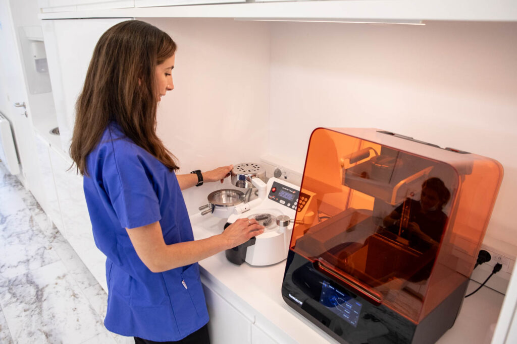 Assistante en orthodontie préparant des appareils dentaires avec thermoformeuse à gouttières et imprimante 3D au laboratoire du cabinet.