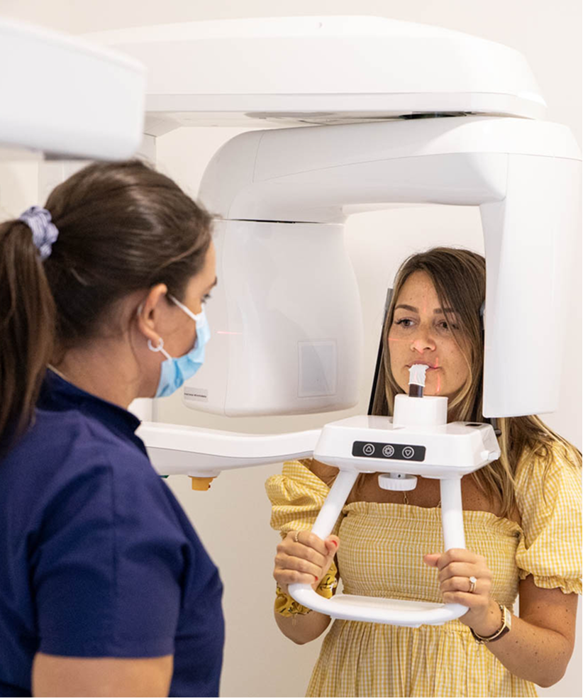 Patiente réalisant une radiographie panoramique dentaire (orthopantomogramme) sous la supervision d’une assistante en cabinet d’orthodontie.